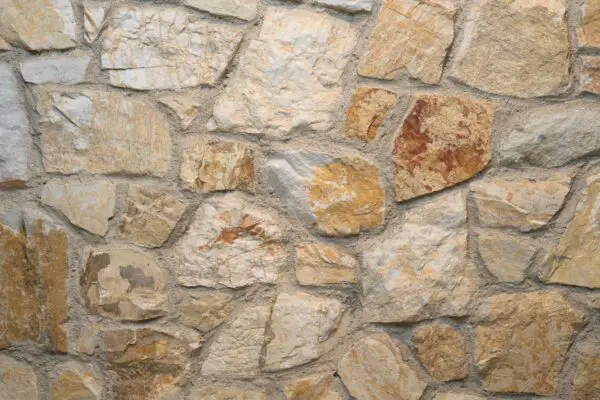 ROCKS Melan: natuurstenen wand in warme beige-, zand- en okertinten met ruwe structuur en zichtbare voegen.