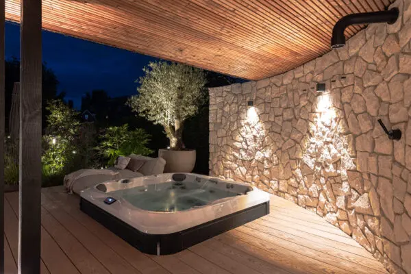 Jacuzzi onder overkapping met natuurstenen wand en warme buitenverlichting in een luxe tuin.