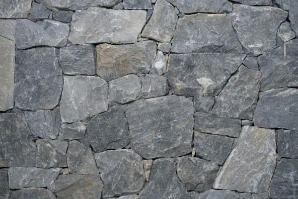 Close-up van een natuurstenen muur met onregelmatige grijze stenen en donkere voegen.