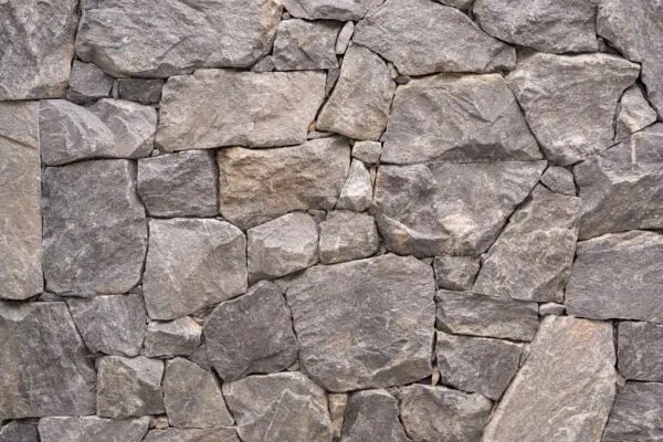 Donkergrijze natuurstenen wand met grote, hoekige stenen in wildverband.