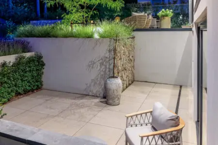 Buitenruimte met strak terras en verticale natuursteen wand, sfeervol verlicht in de avond.