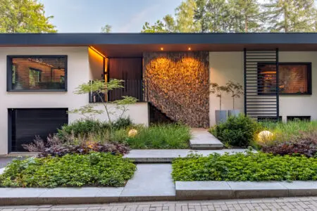 Moderne woning met verticale natuursteen gevel bij de entree, gecombineerd met strakke lijnen, groen en subtiele buitenverlichting.