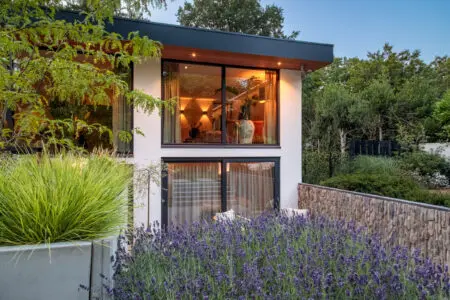Gevel van moderne woning met verticale natuursteen en grote raampartijen, waarbij binnen en buiten visueel in elkaar overlopen.