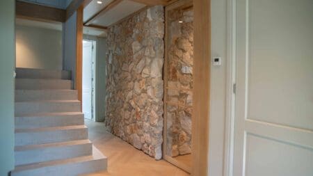 Hal en trap langs een wand met Rocks Grey natuursteenstrips en schuifdeur